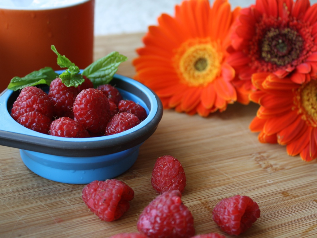 Свежая малина на столе с цветами герберы