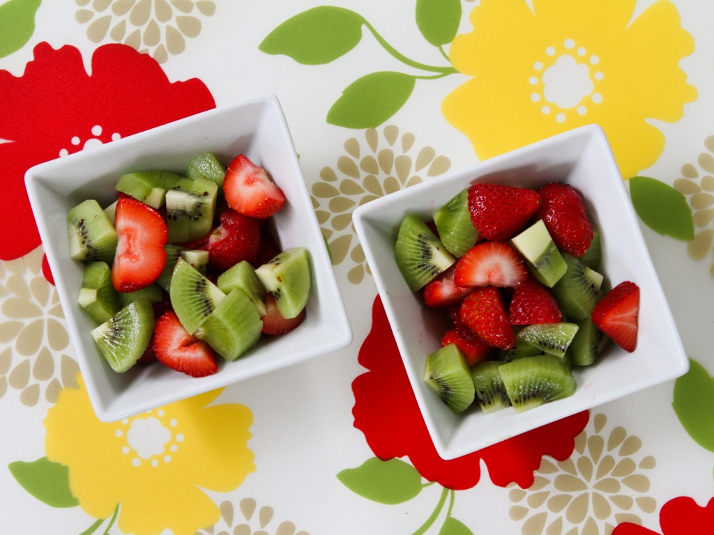 Салат с ягодами клубники и киви в белых тарелках на столе 