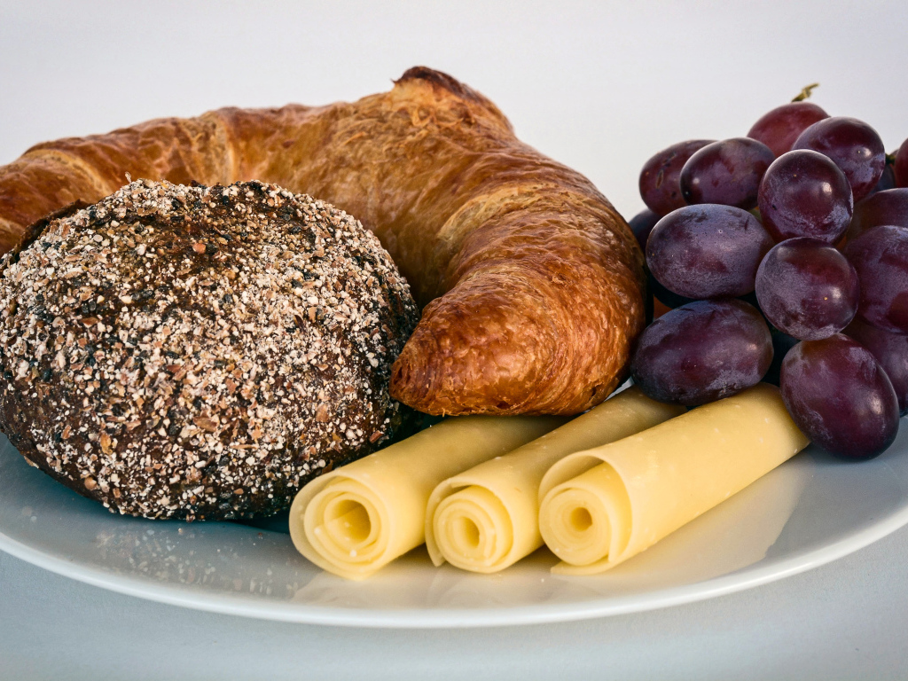 Свежая выпечка с сыром и розовым виноградом на белой тарелке 