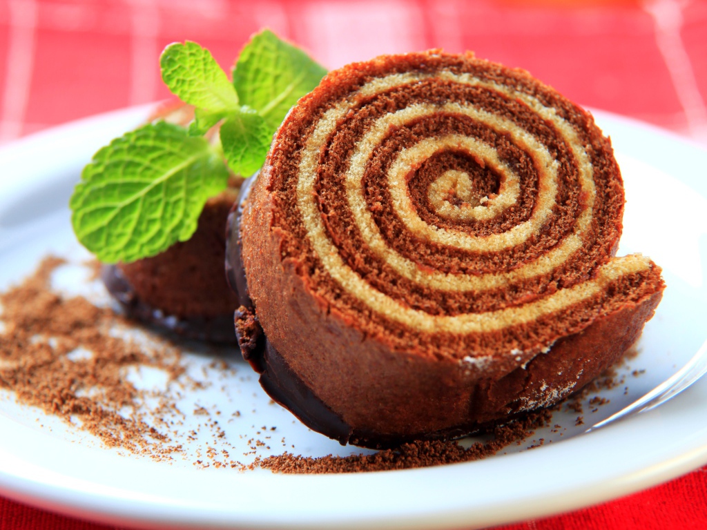 Кусок сладкого рулета с шоколадом и листом мяты на тарелке