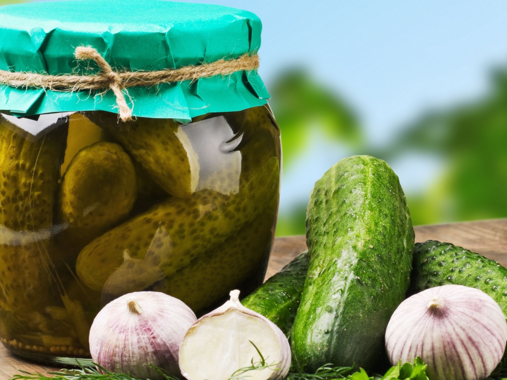Консервированные огурцы в банке на столе со свежими огурцами и чесноком