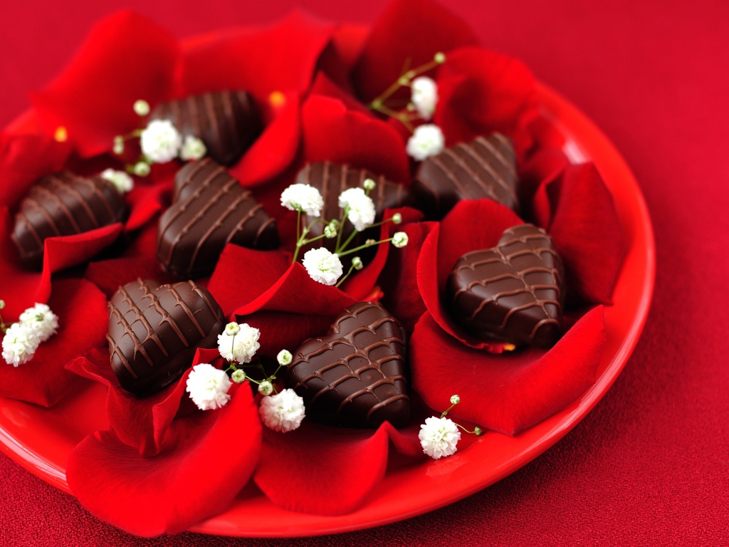 Шоколадные конфеты в форме сердца на тарелке с лепестками розы