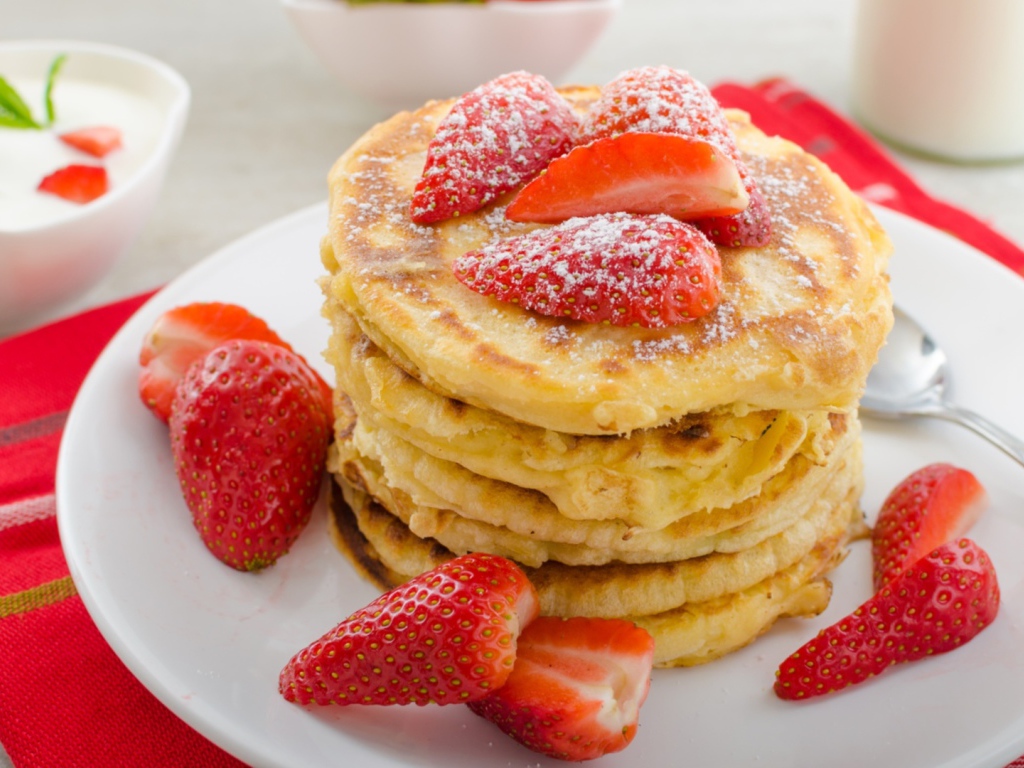 Оладьи с клубникой и сахарной пудрой на белой тарелке 