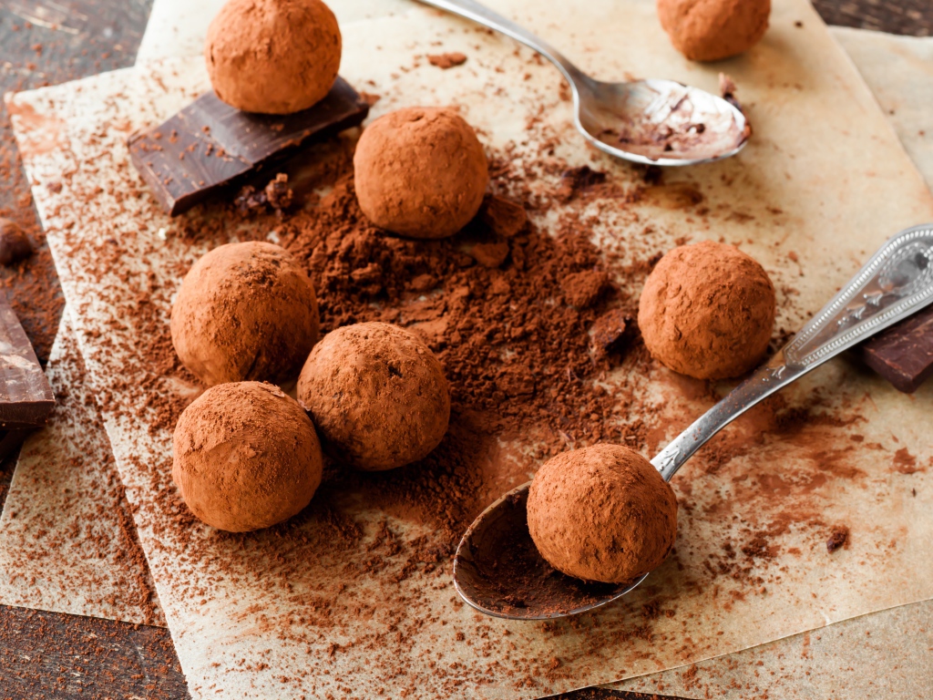 Круглые шоколадные конфеты в какао на столе с ложками