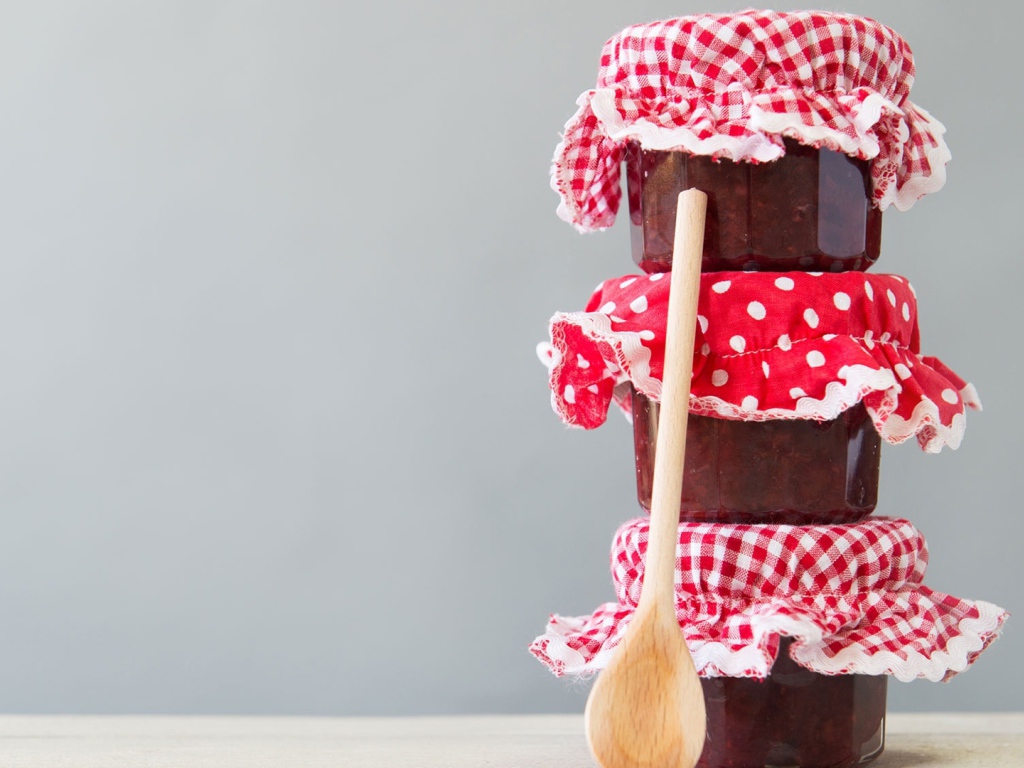 Три баночки варенья с деревянной ложкой на сером фоне