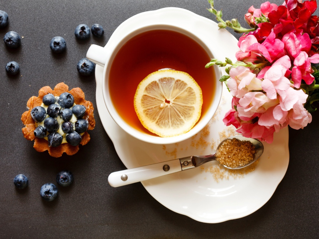 Чашка чая с лимоном на столе с кексом и цветами