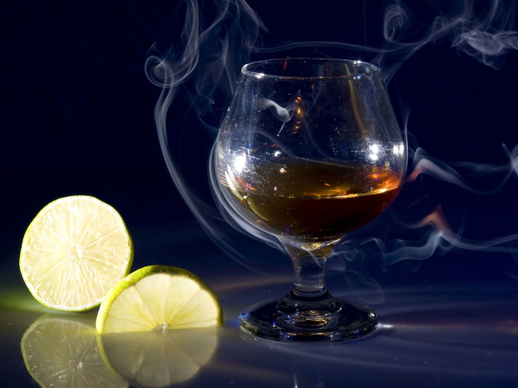 Бокал коньяка в дыму с кусочками лимона