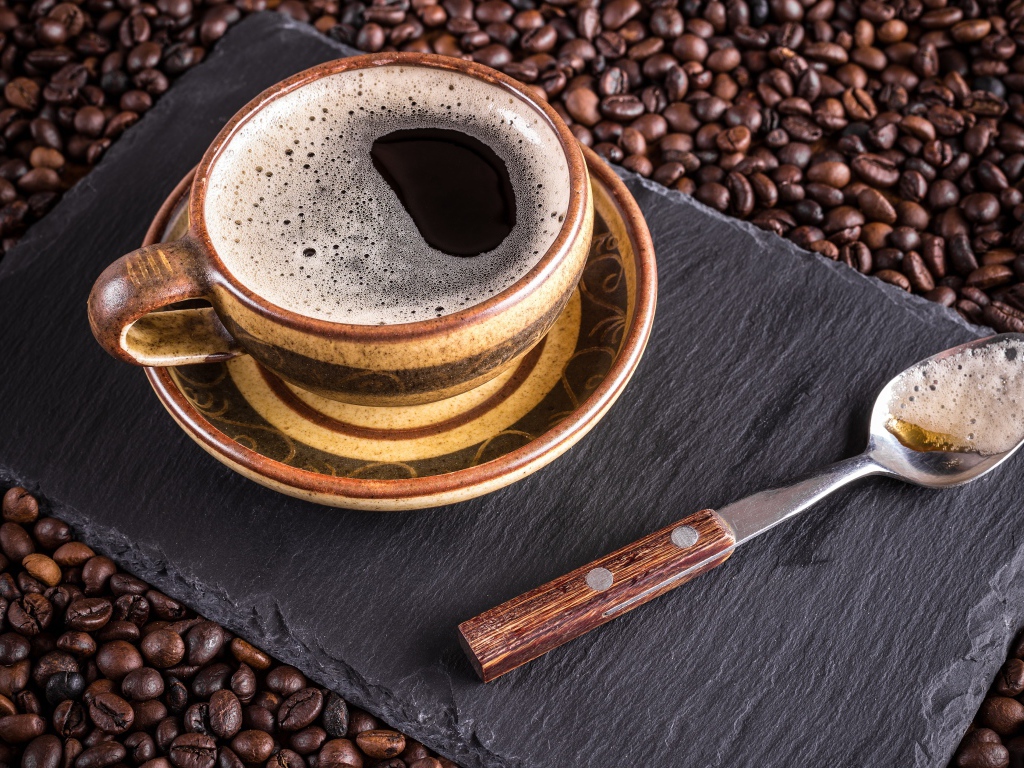 Большая чашка кофе с чайной ложкой стоят на кофейных зернах