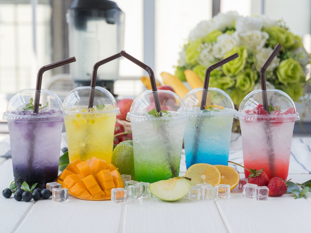 Коктейли в стаканах с трубочками на столе с кубиками льда и фруктами