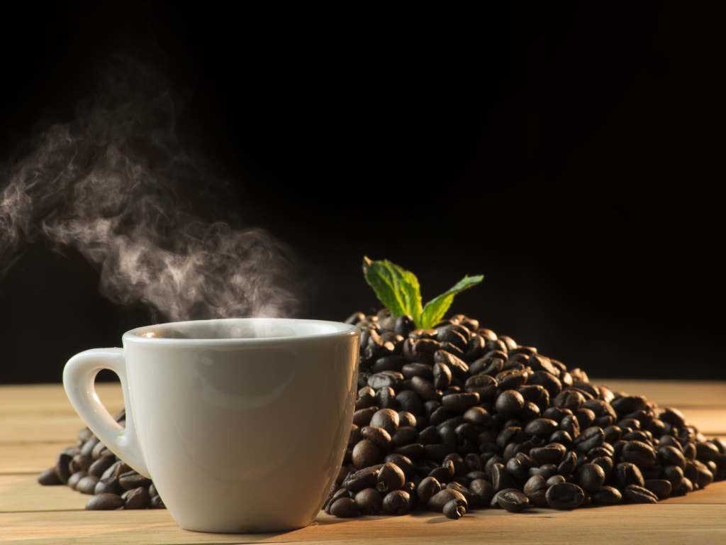 Кофейные зерна на столе с чашкой горячего кофе 