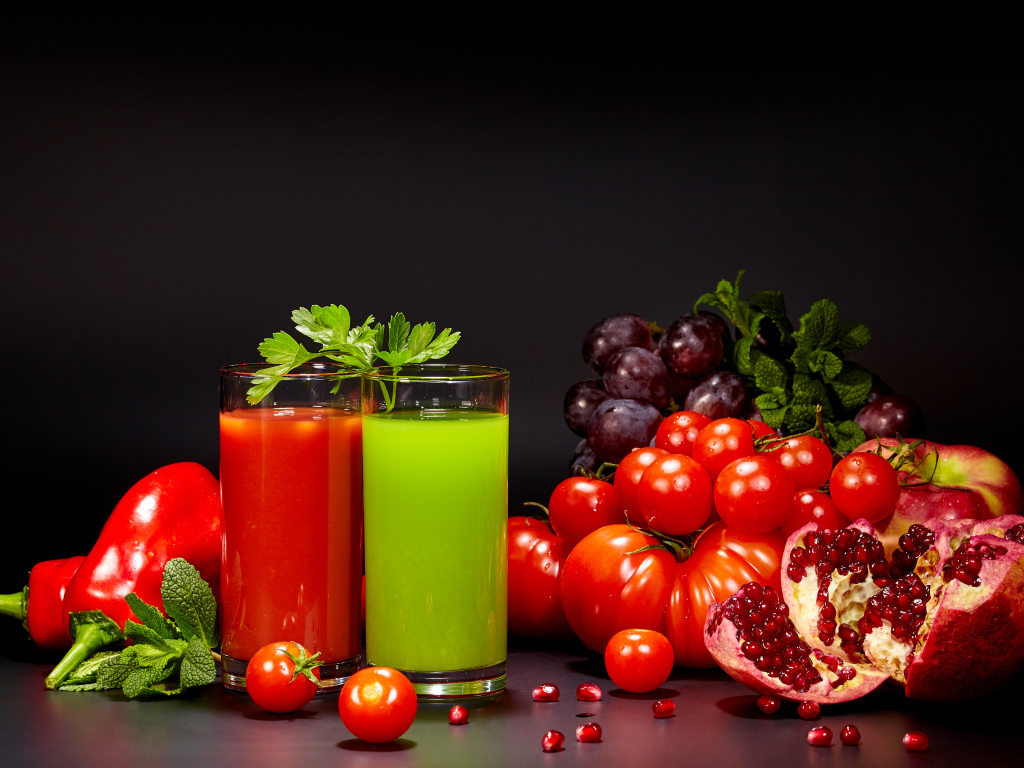 Два стакана сока на столе со свежими помидорами, перцем, гранатом, виноградом и зеленью
