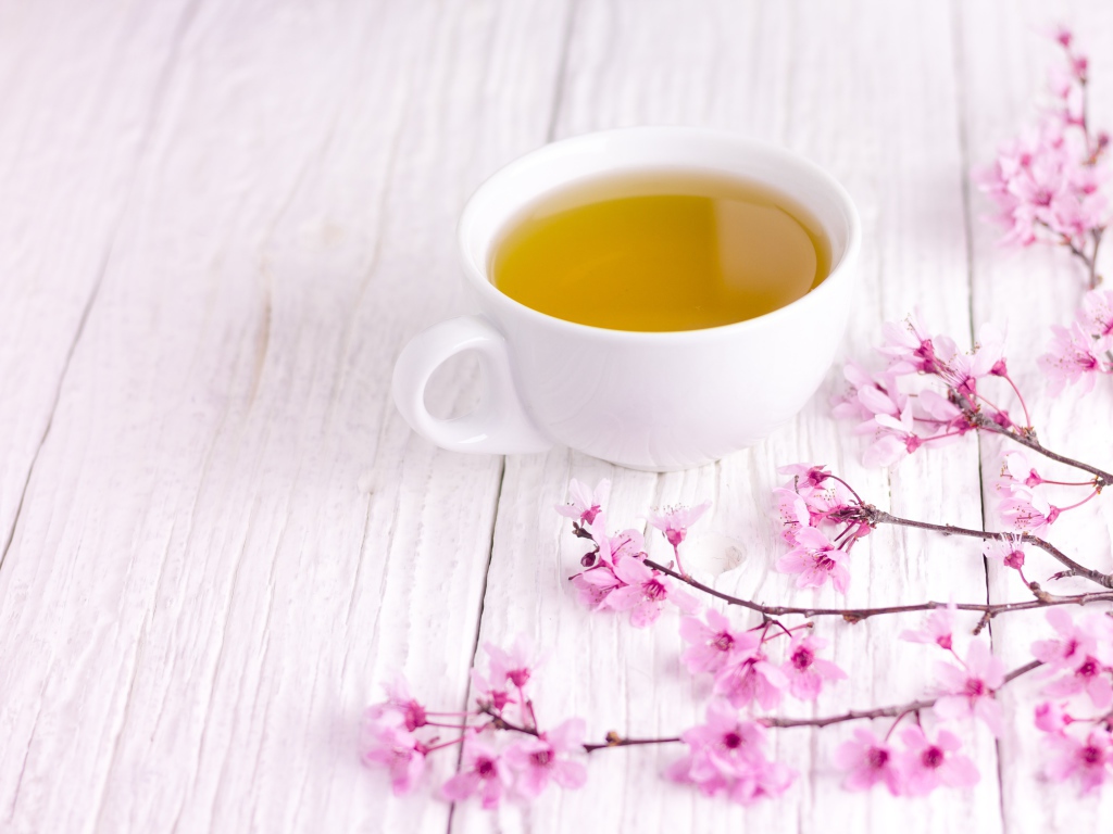 Белая чашка зеленого чая на столе с розовыми цветами