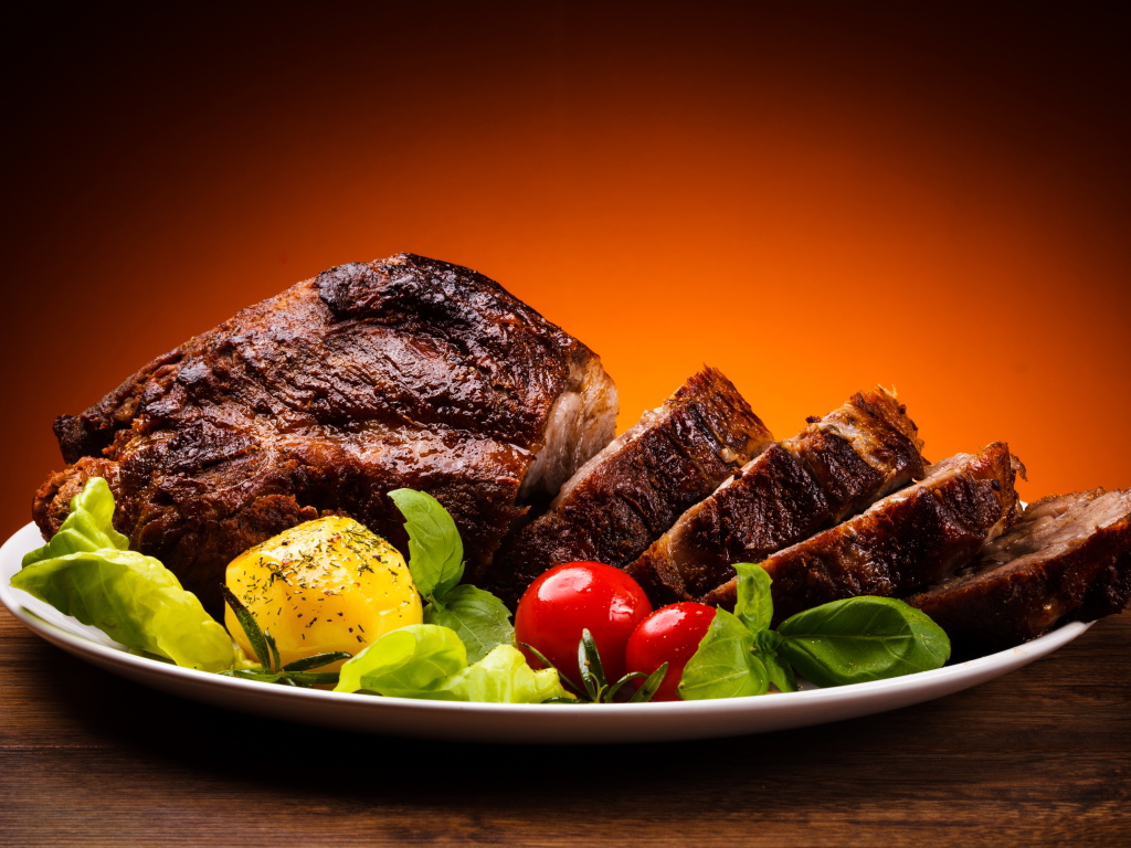 Кусок жареного мяса на тарелке с картофелем и помидорами 