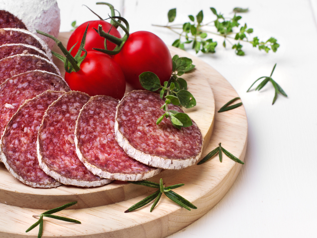 Вкусная колбаса на разделочной доске с помидорами и зеленью 