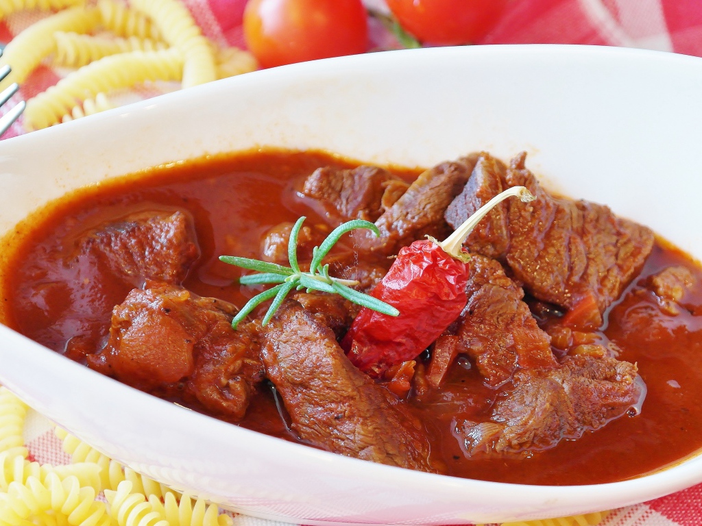 Мясной гуляш в белой тарелке с острым перцем