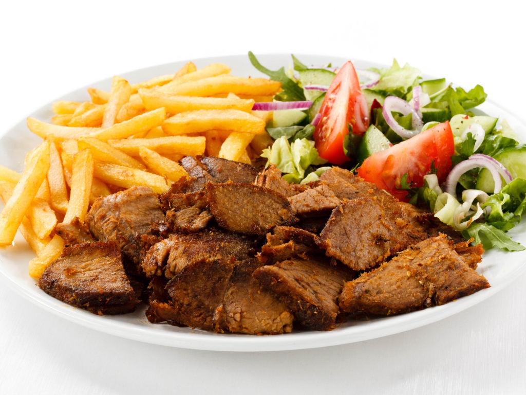 Кусочки мяса на тарелке с картофелем фри и салатом