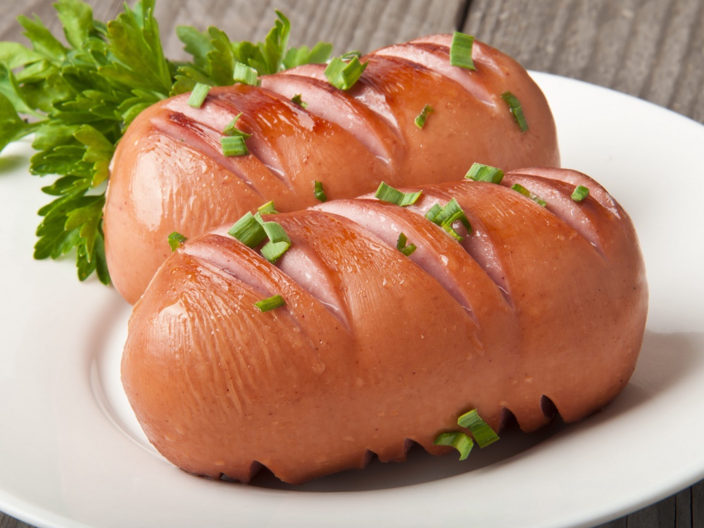 Два жареные сардельки на большой белой тарелке с зеленью 