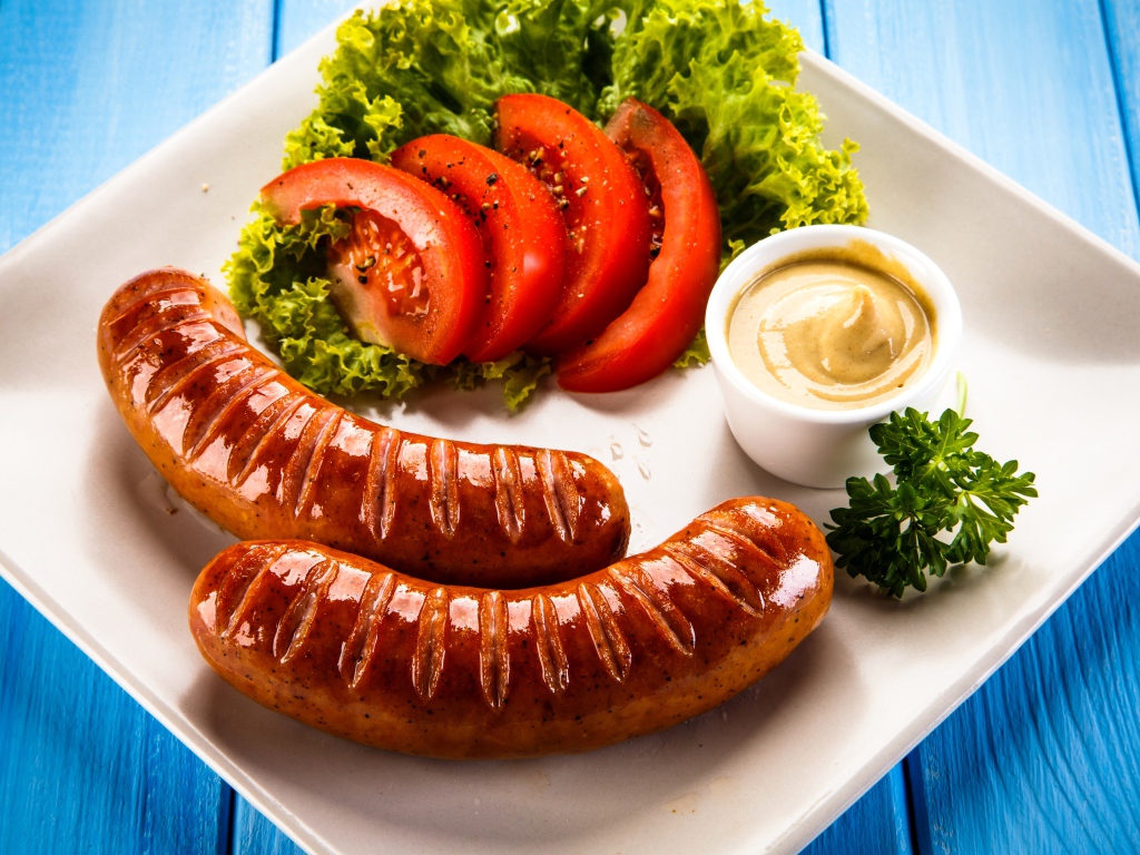 Две сосиски гриль на тарелке с овощами и горчицей