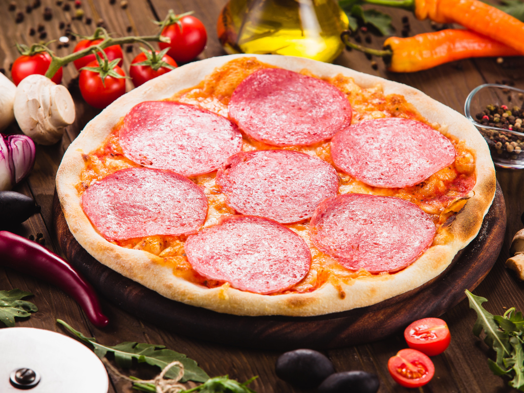 Пицца с салями на столе с овощами 