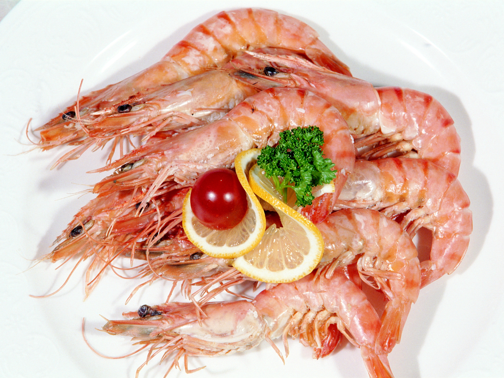 Креветки с лимоном и помидором на белой тарелке
