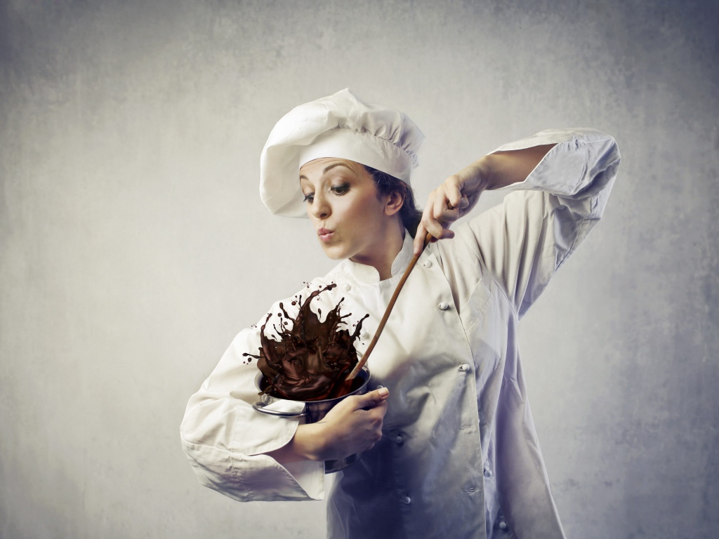 Женщина повар мешает шоколад в посуде на сером фоне