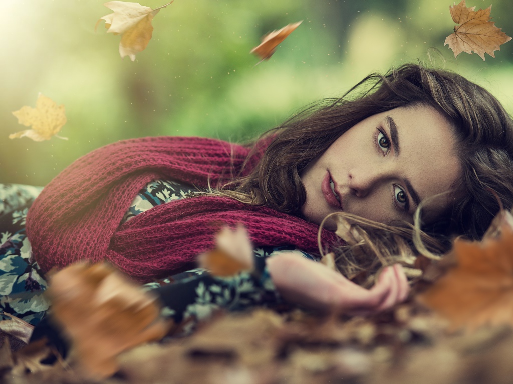 Красивая шатенка в красном шарфе лежит на сухой листве