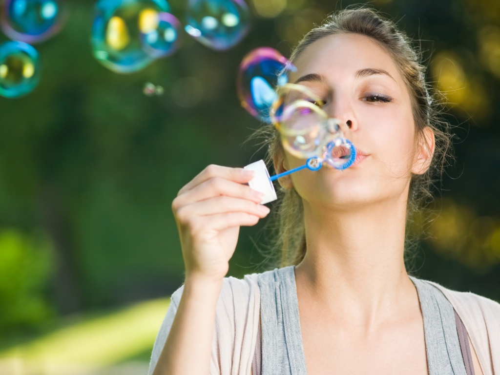 Милая молодая девушка пускает мыльные пузыри
