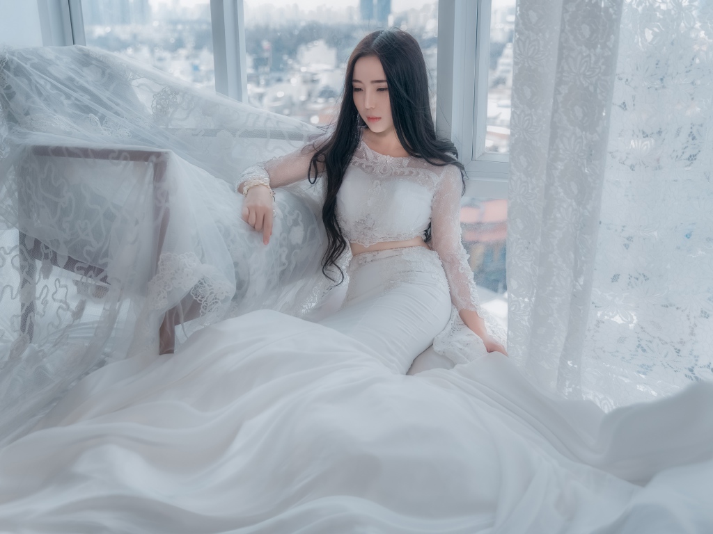 Красивая азиатка в белом свадебном платье сидит на полу