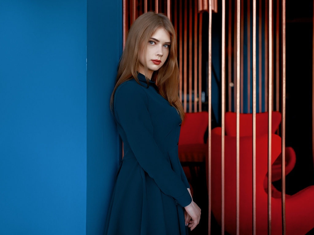 Красивая голубоглазая девушка стоит в пальто у стены