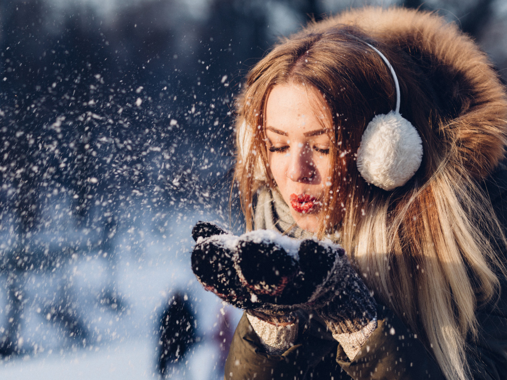Красивая девушка сдувает снег с ладоней зимой