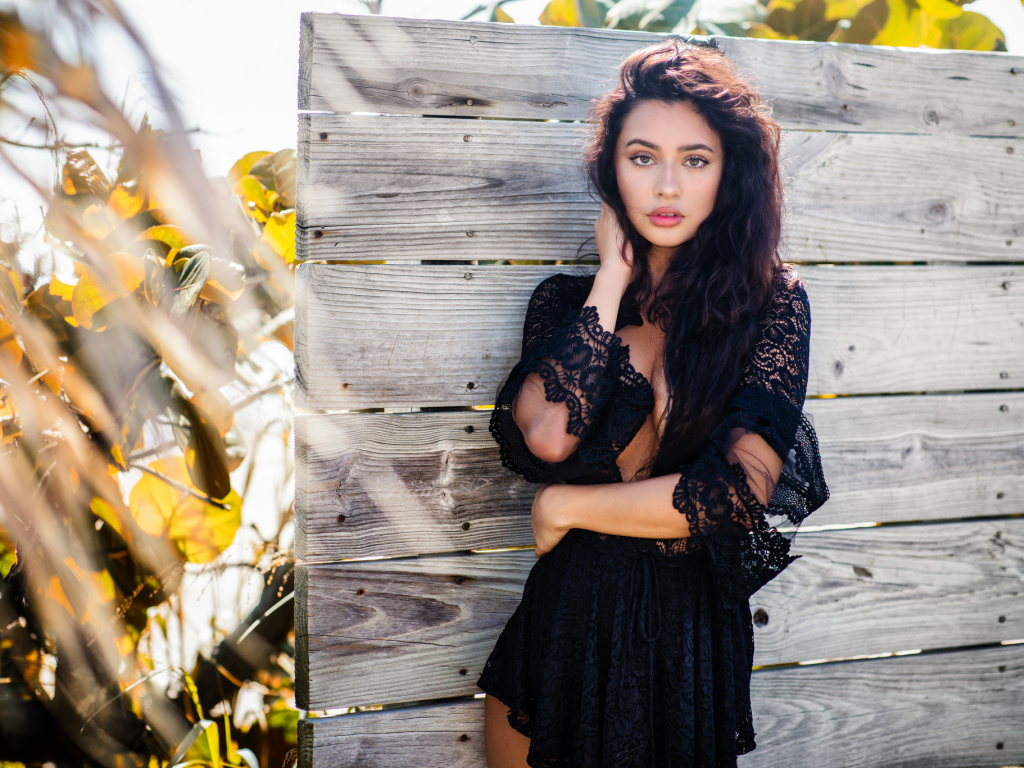 Красивая девушка в черном платье у стены 