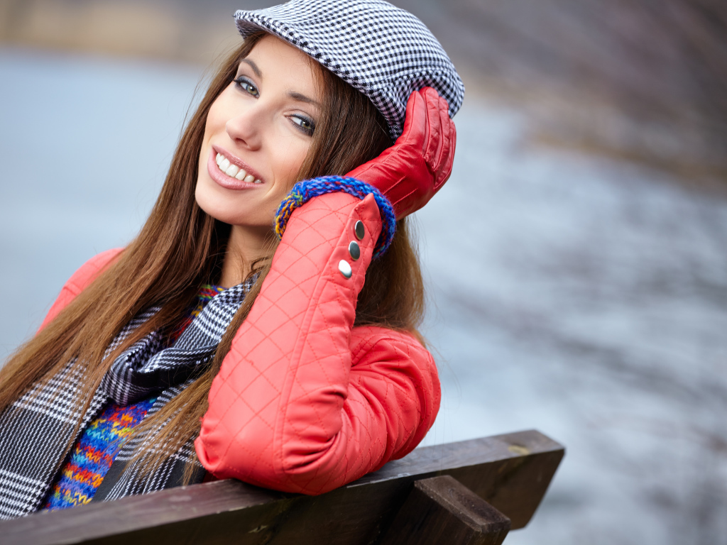 Красивая девушка в красной куртке сидит на лавке