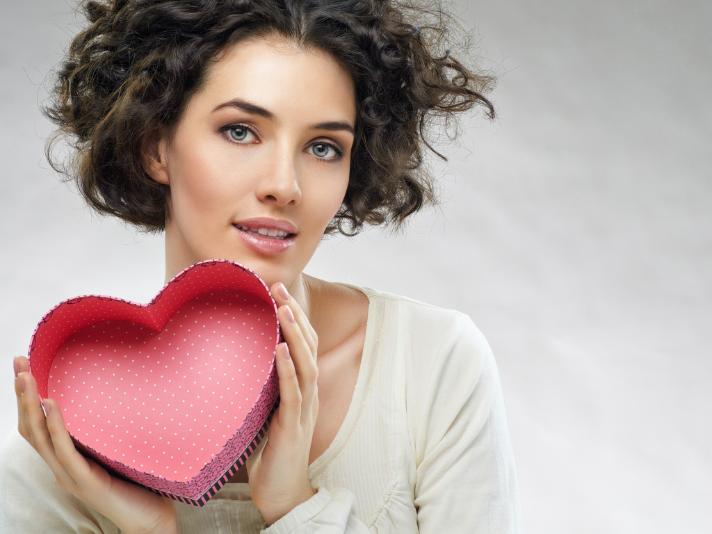 Красивая девушка с коробкой в форме сердца в руках на сером фоне