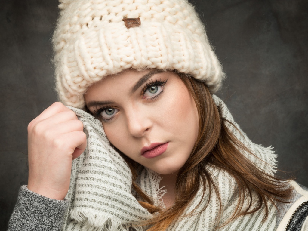 Красивая зеленоглазая девушка в белой вязаной шапке с шарфом