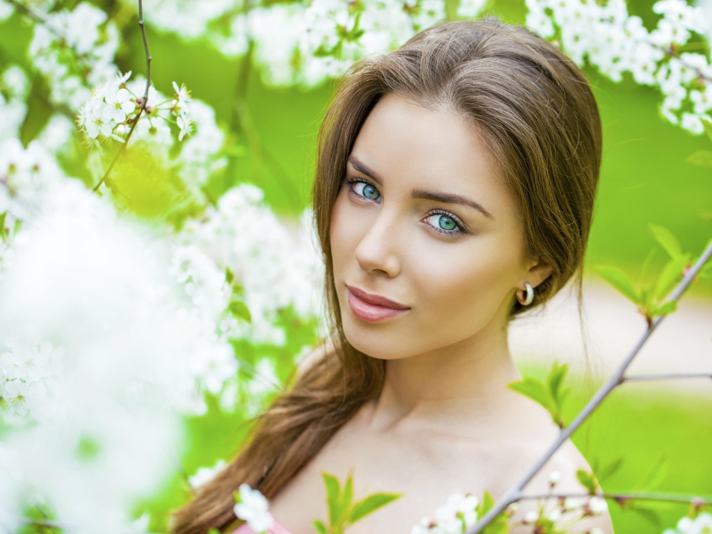 Красивая зеленоглазая девушка у цветущей вишни 
