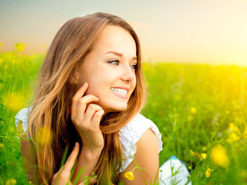 Красивая улыбающаяся молодая девушка лежит в зеленой траве