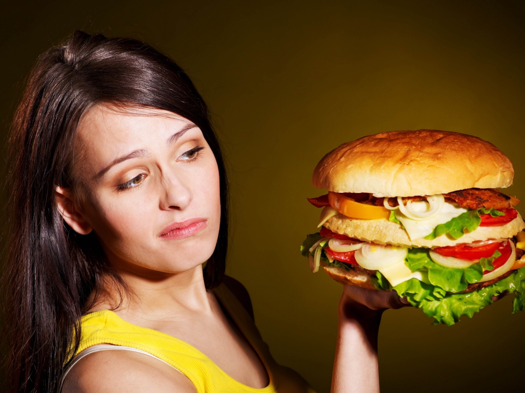 Недовольная девушка с большим гамбургером в руках 