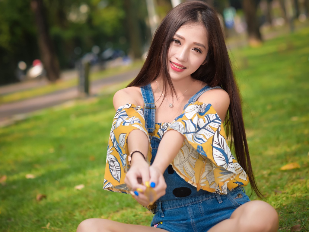 Улыбающаяся девушка азиатка сидит на траве