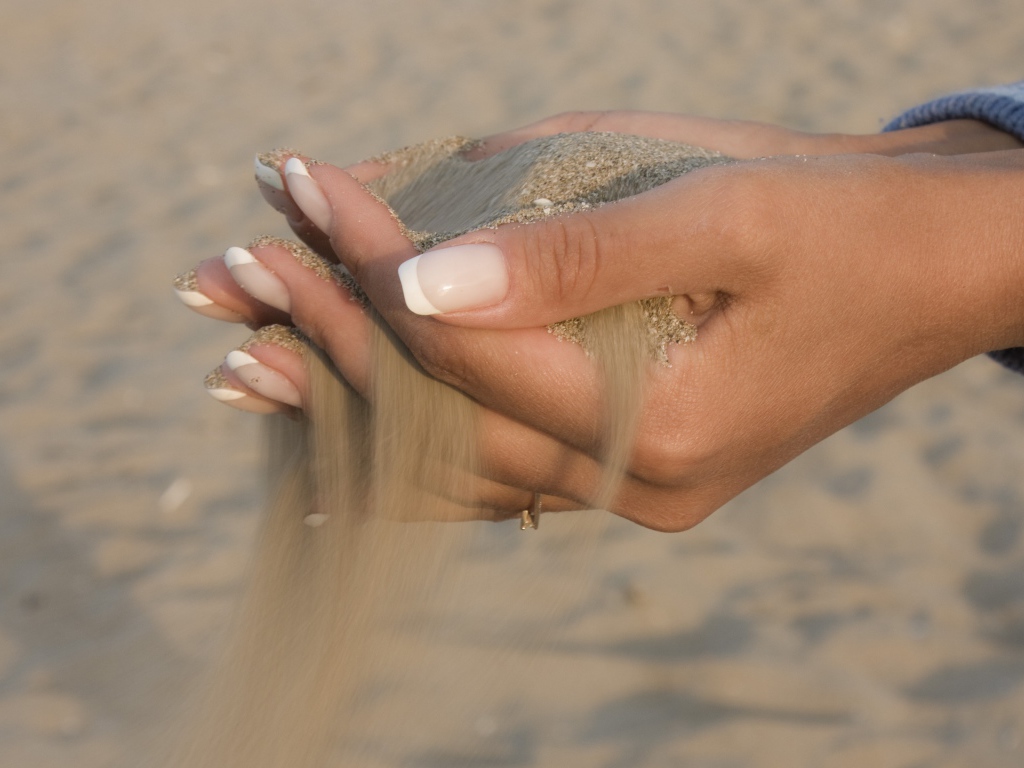 Желтый песок в руках у девушки с красивым маникюром