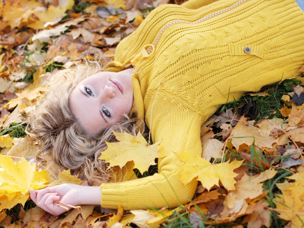 Молодая блондинка лежит на сухой листве осенью