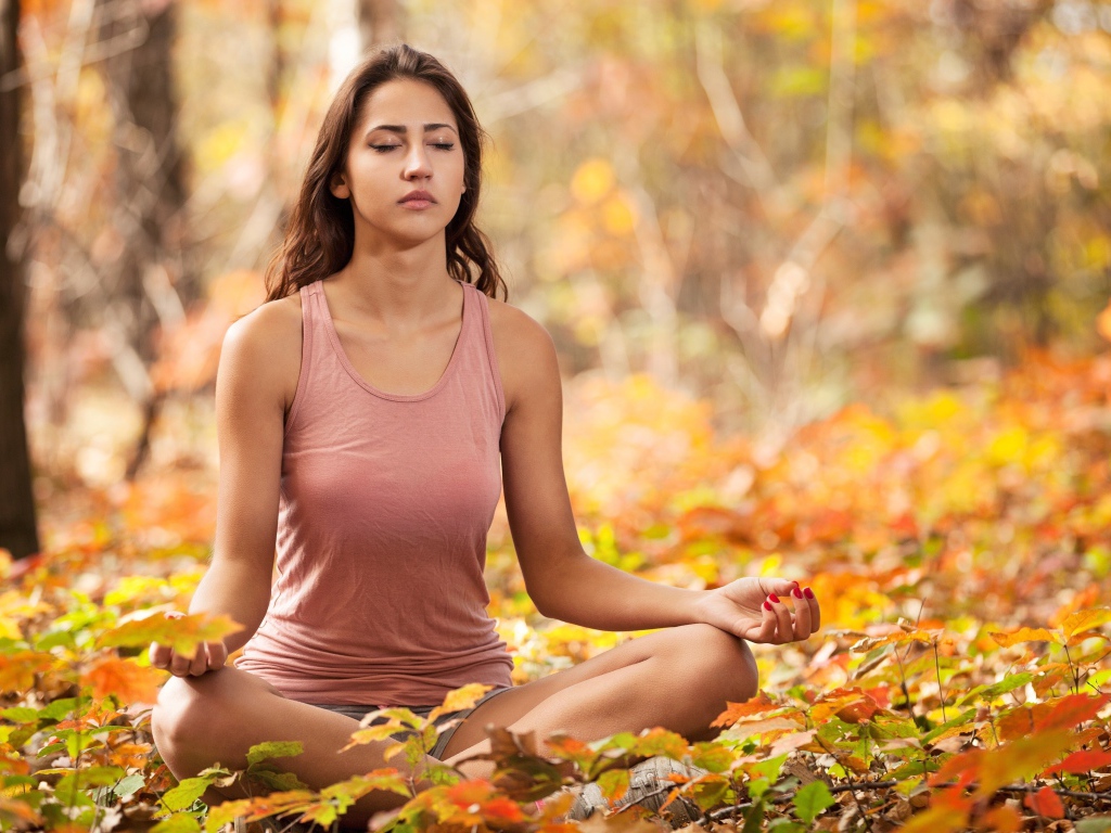 Молодая девушка медитирует в лесу сидя на земле
