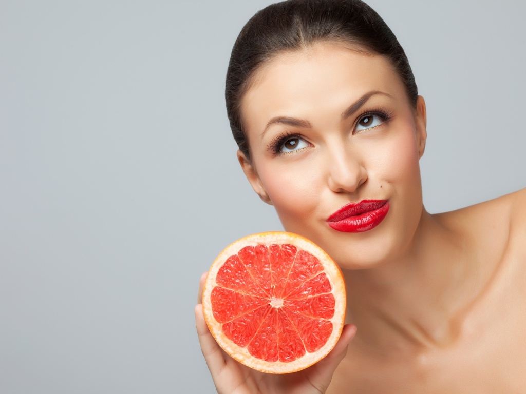 Молодая девушка с красными губами с половиной грейпфрута