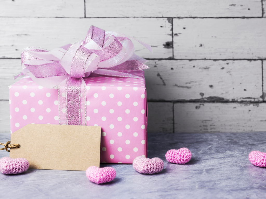 Большая сиреневая подарочная коробка с бантом и маленькими сердечками на фоне стены
