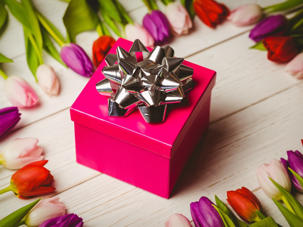 Красная коробка с подарком на столе с тюльпанами