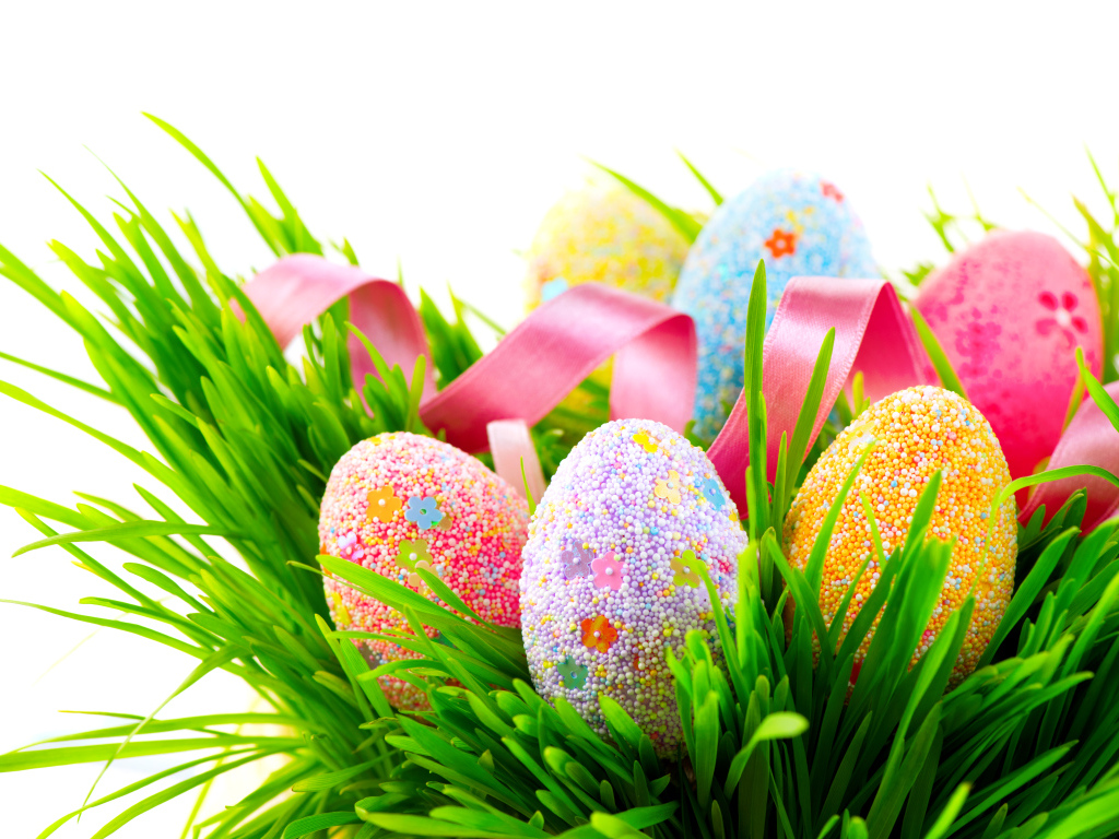 Пасхальные яйца в зеленой траве с розовой лентой на белом фоне