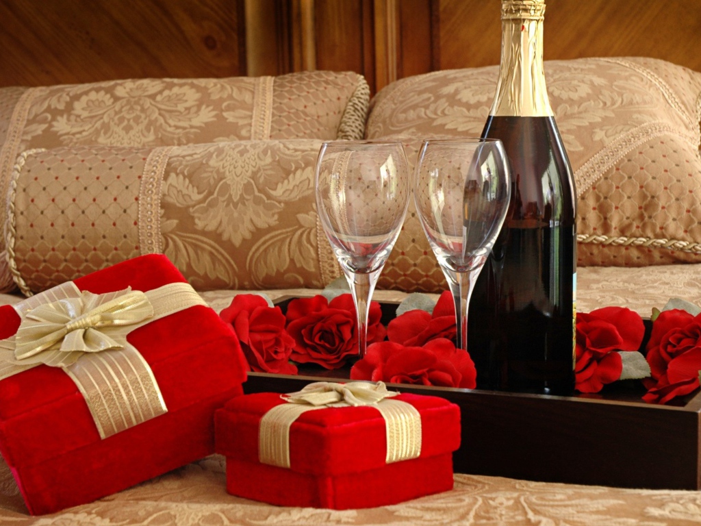 Бутылка вина, два бокала и подарки для романтического вечера на кровати 