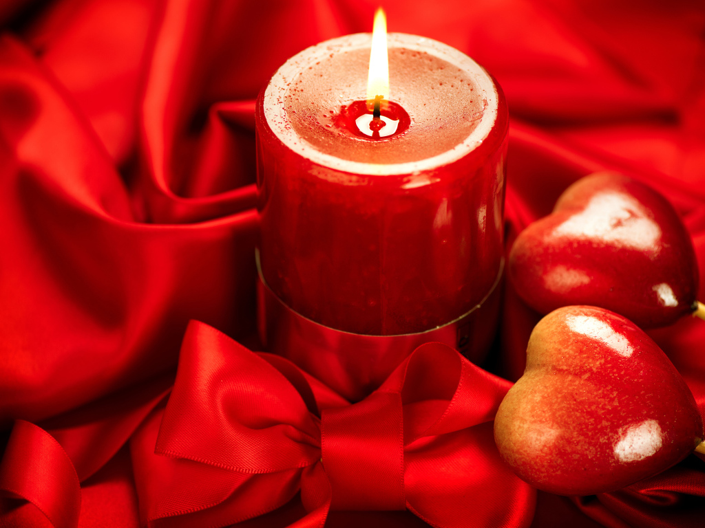 Зажженная свеча с двумя сердечками на красном фоне с бантом