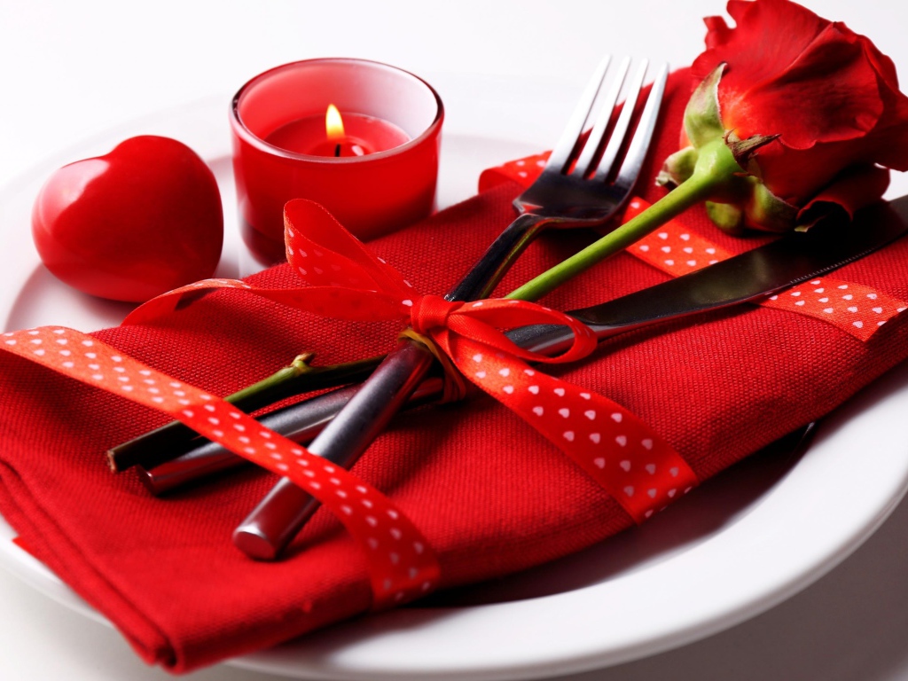 Роза, столовые приборы и зажженная свеча на белой тарелке 