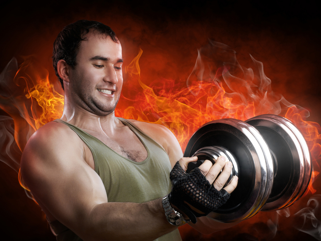 A man sportsman holds a dumbbell in front of a fire