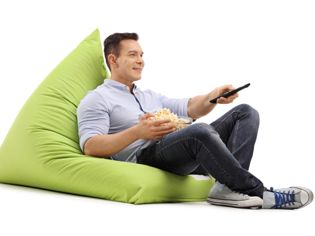 Мужчина с попкорном и пультом от телевизора лежит на зеленой подушке